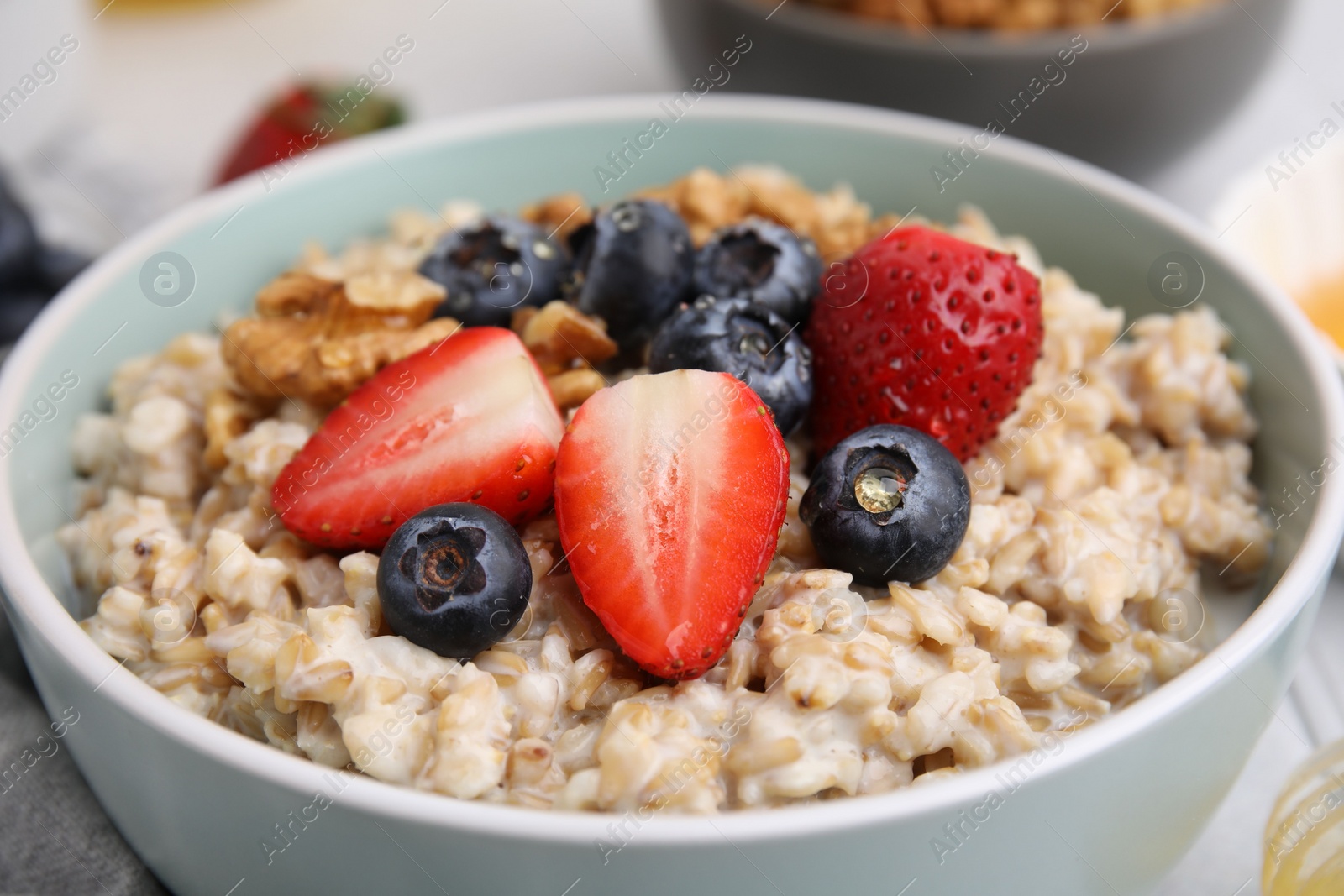 Photo of Tasty oatmeal with strawberries, blueberries and walnuts in bowl on grey table, closeup