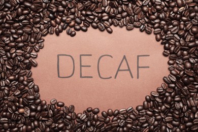 Photo of Word Decaf and coffee beans on brown background, top view