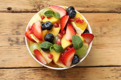 Tasty fruit salad in bowl on wooden table, top view