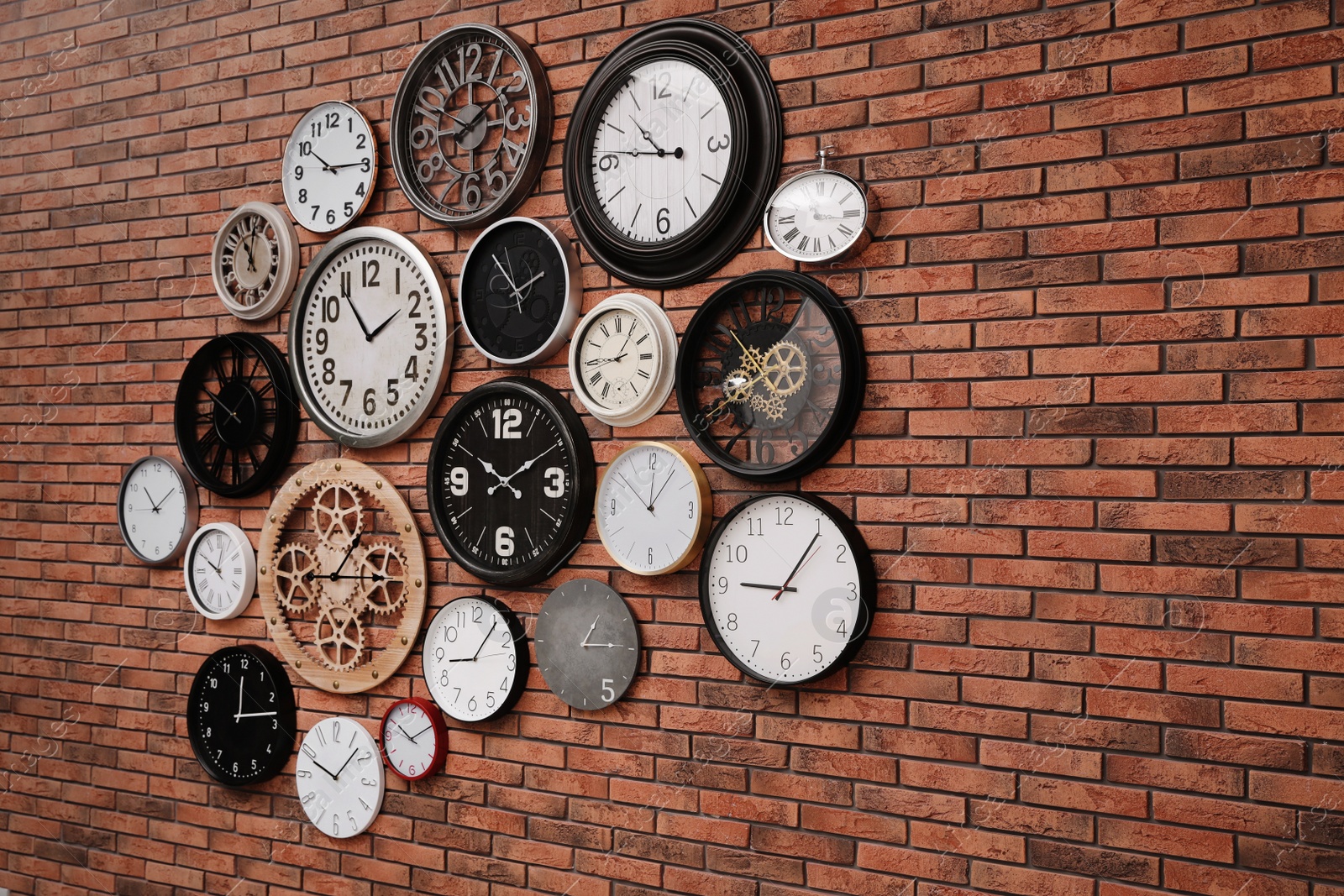 Photo of Collection of clocks hanging on red brick wall