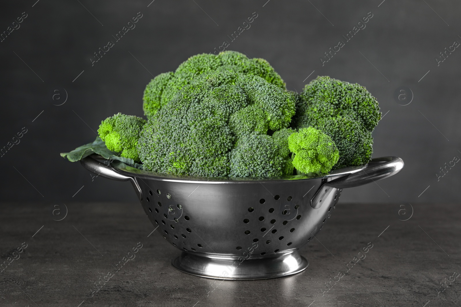 Photo of Colander with fresh raw broccoli on grey table