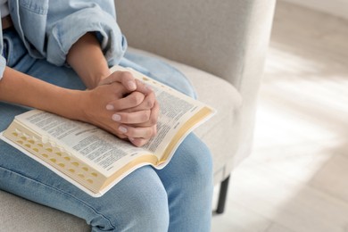Photo of Religious woman with Bible praying indoors, closeup. Space for text