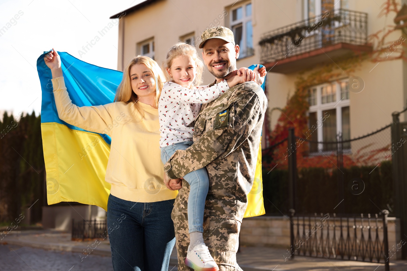 Photo of Soldier in military uniform reunited with his family and Ukrainian flag on city street