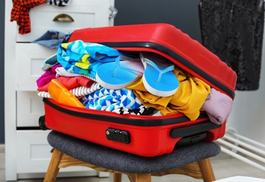 Photo of Suitcase with beach clothes and accessories on stool indoors