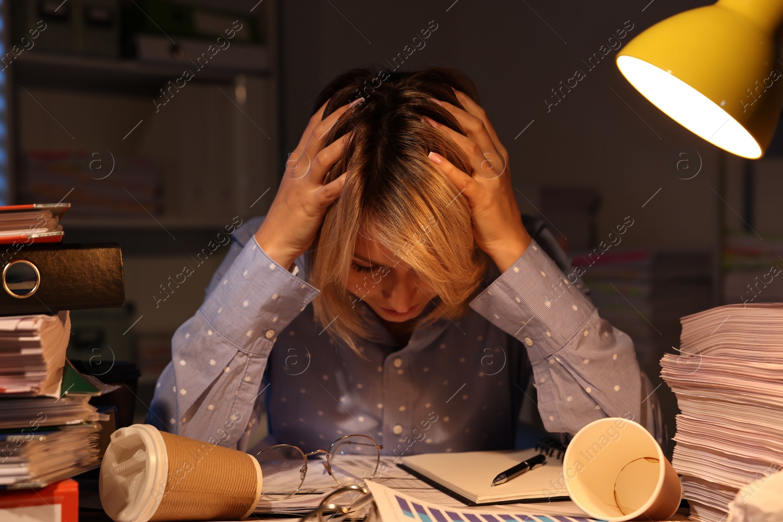 Photo of Overwhelmed woman surrounded by documents and paper coffee cups at table in office at night