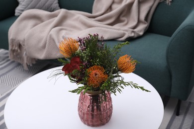 Photo of Vase with bouquet of beautiful leucospermum flowers on white coffee table in living room