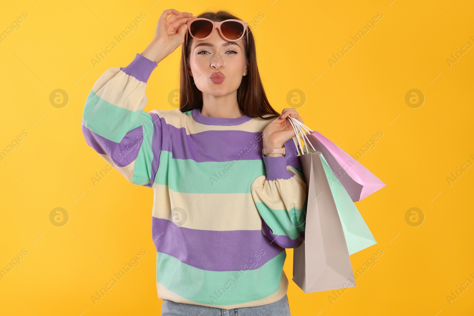 Photo of Beautiful young woman with shopping bags on yellow background. Big sale