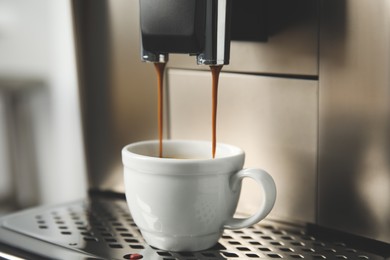 Photo of Espresso machine pouring coffee into cup against blurred background, closeup