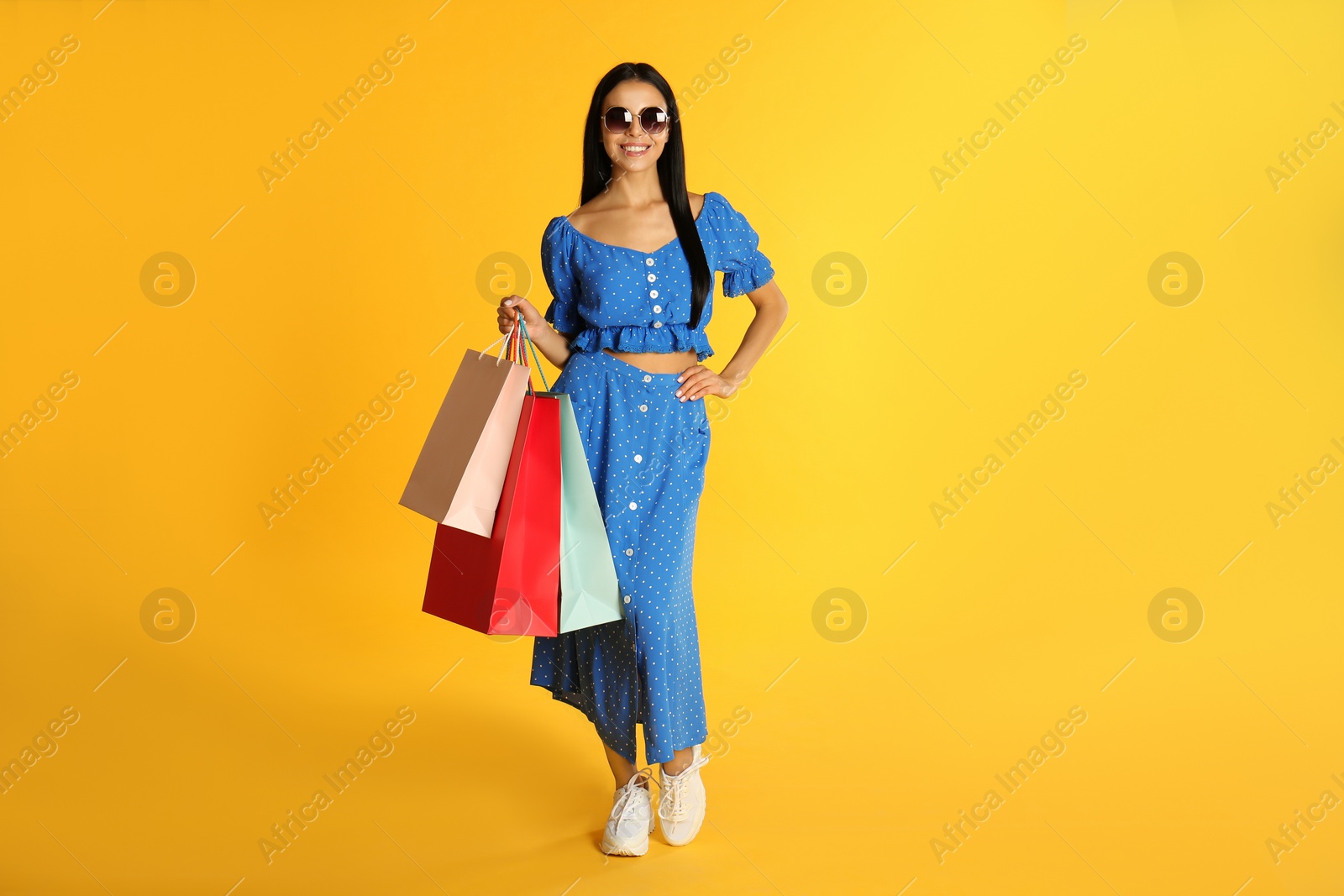 Photo of Beautiful young woman with paper shopping bags on yellow background