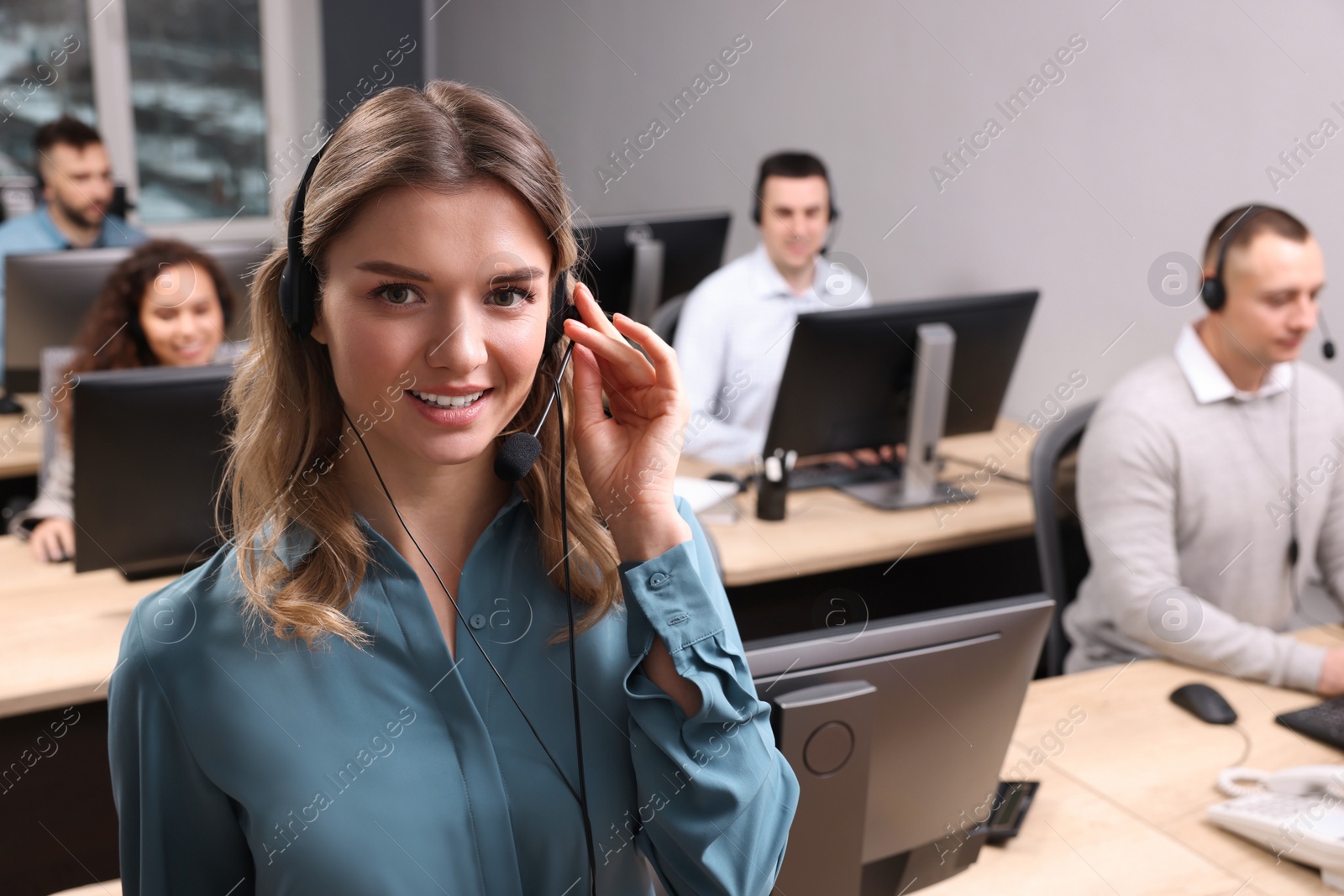 Photo of Call center operators working in modern office, focus on young woman with headset