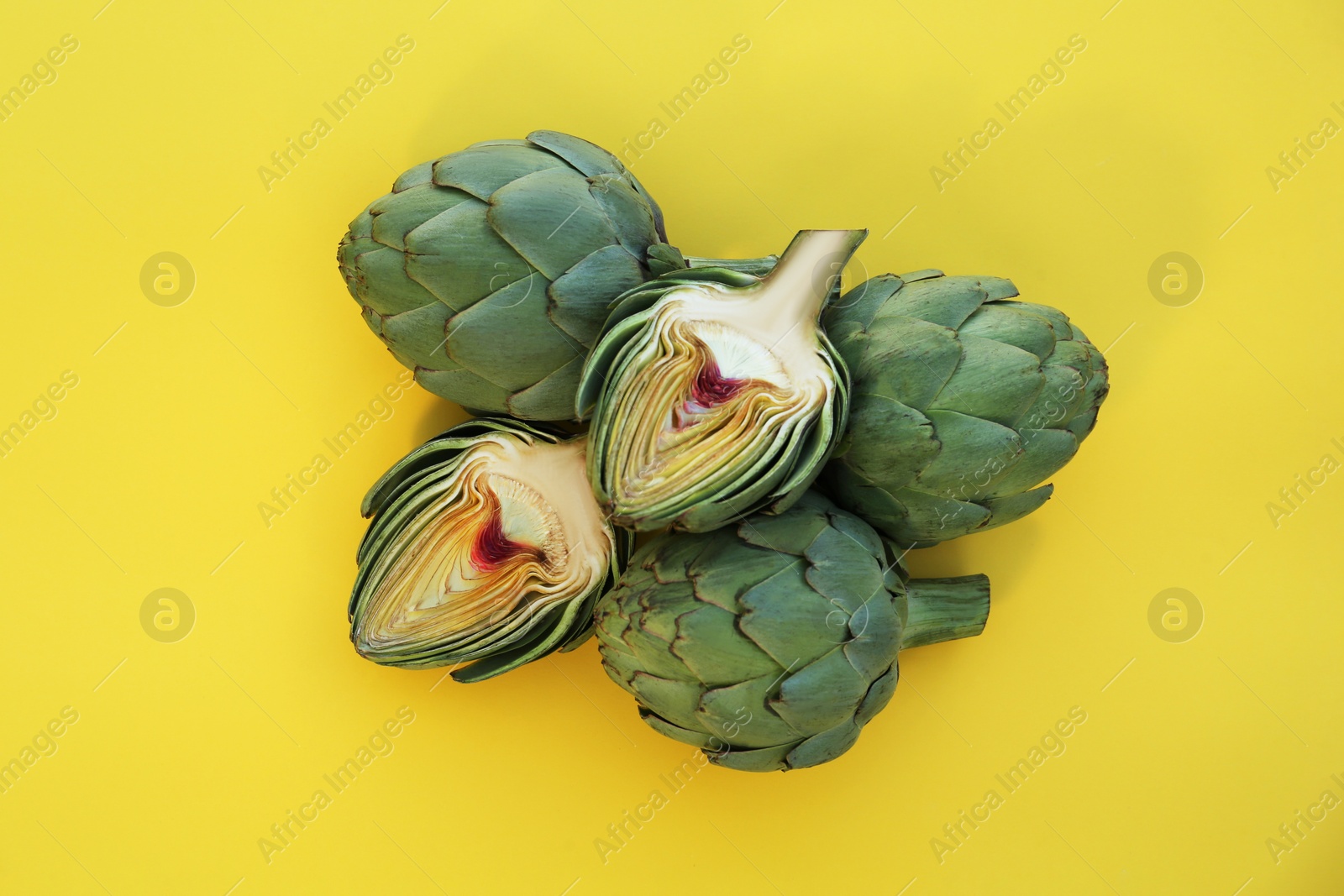 Photo of Cut and whole fresh raw artichokes on yellow background, flat lay