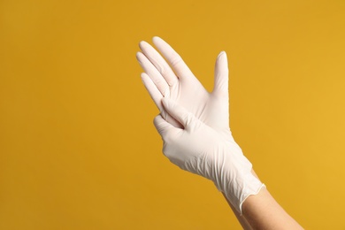 Doctor wearing medical gloves on yellow background, closeup. Space for text