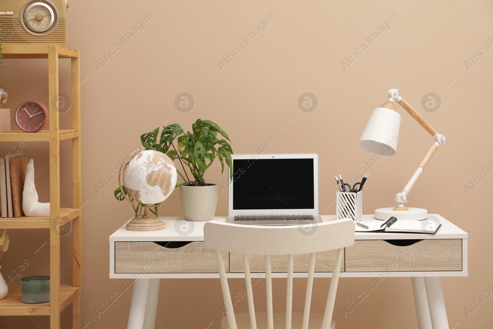 Photo of Cozy workplace with modern laptop on desk and comfortable chair at home