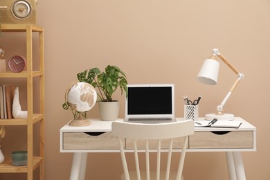 Photo of Cozy workplace with modern laptop on desk and comfortable chair at home