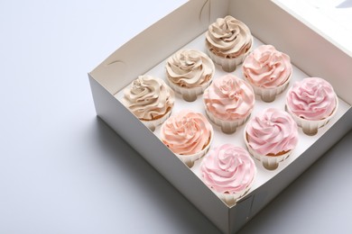 Photo of Tasty cupcakes in box on white background, closeup. Space for text