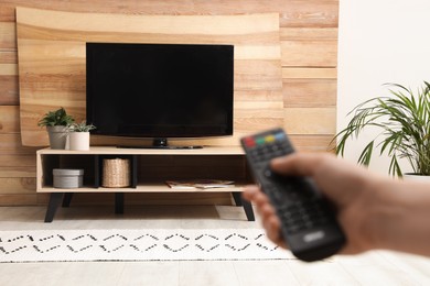 Photo of Young man switching channels on TV set with remote control at home, closeup