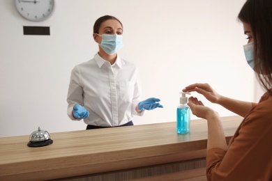 Photo of Woman applying antiseptic gel at hotel reception, closeup