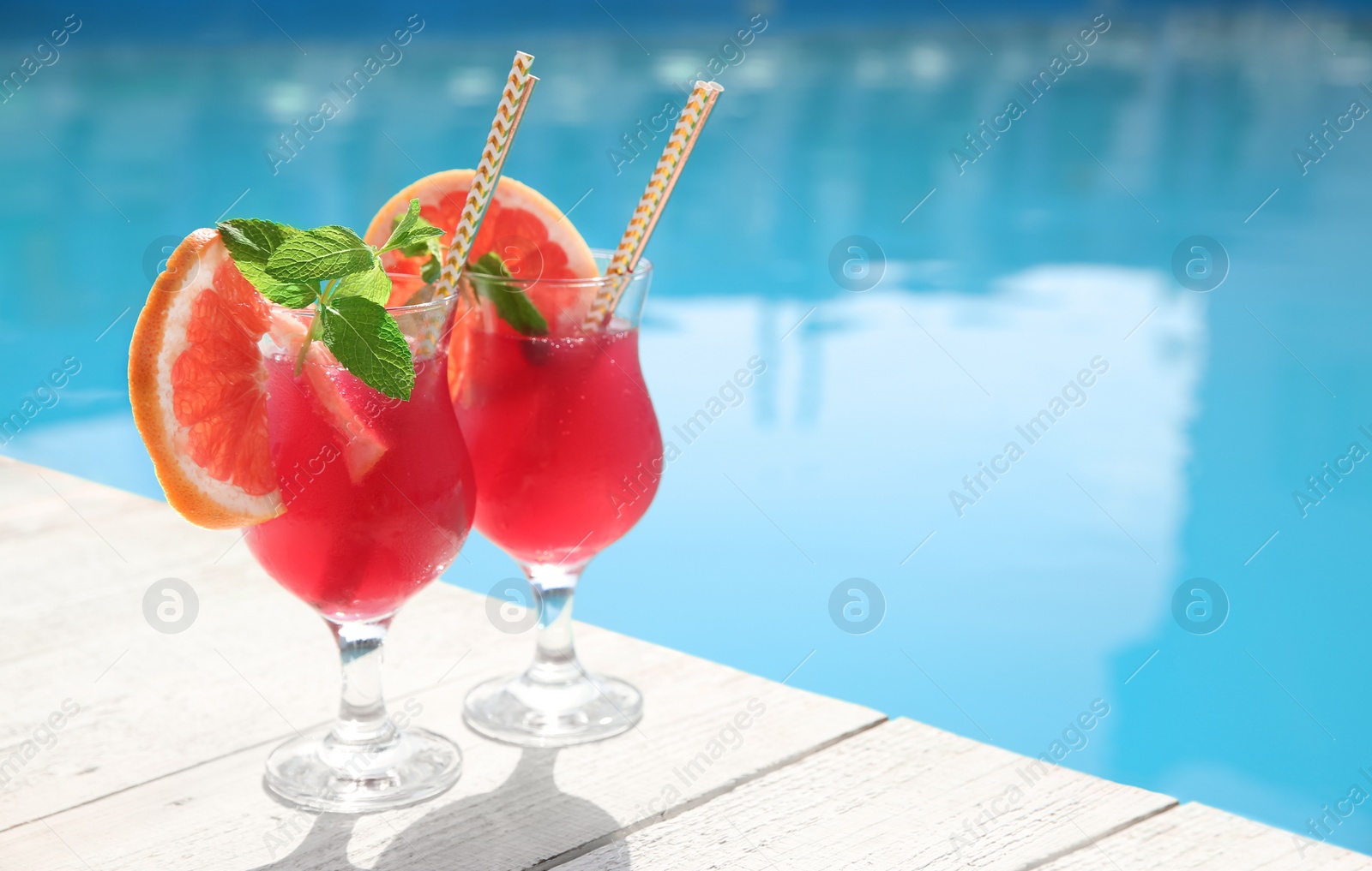 Photo of Refreshing cocktail in glasses near outdoor swimming pool on sunny day. Space for text