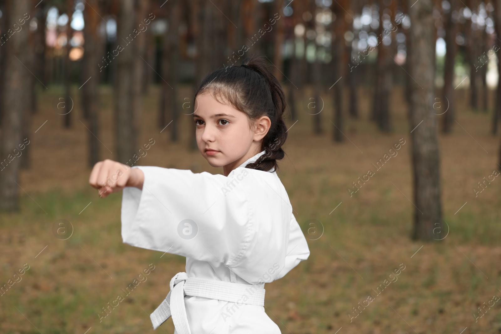 Photo of Cute little girl in kimono practicing karate in forest