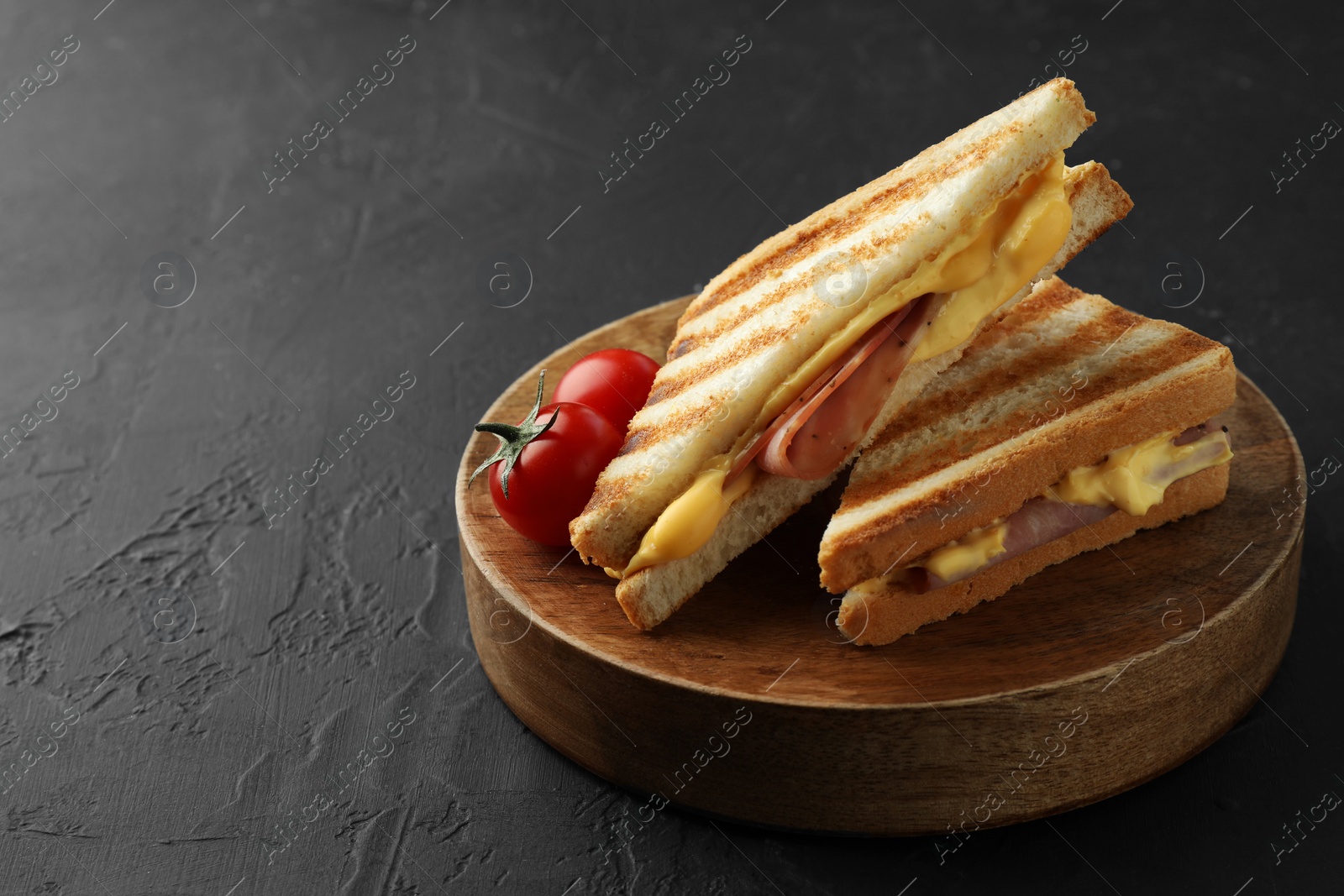 Photo of Tasty sandwiches with ham, melted cheese and tomatoes on black textured table, space for text