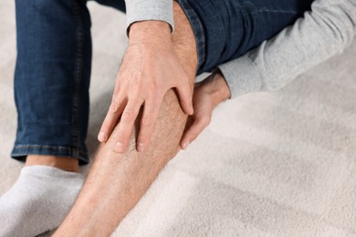 Photo of Man suffering from leg pain on white carpet, closeup