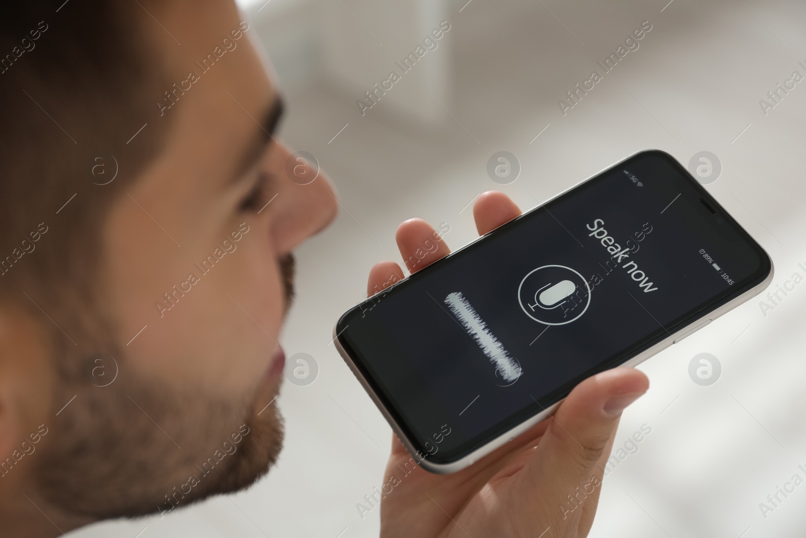 Photo of Young man using voice search on smartphone indoors, closeup