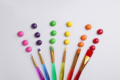 Photo of Creative flat lay composition with paint brushes and colorful candies on light grey background