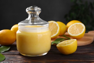 Delicious lemon curd in glass jar, fresh citrus fruits and green leaves on wooden table