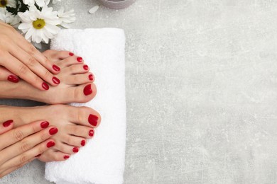 Photo of Woman with stylish red toenails after pedicure procedure and chamomile flowers on grey textured background top view. Space for text