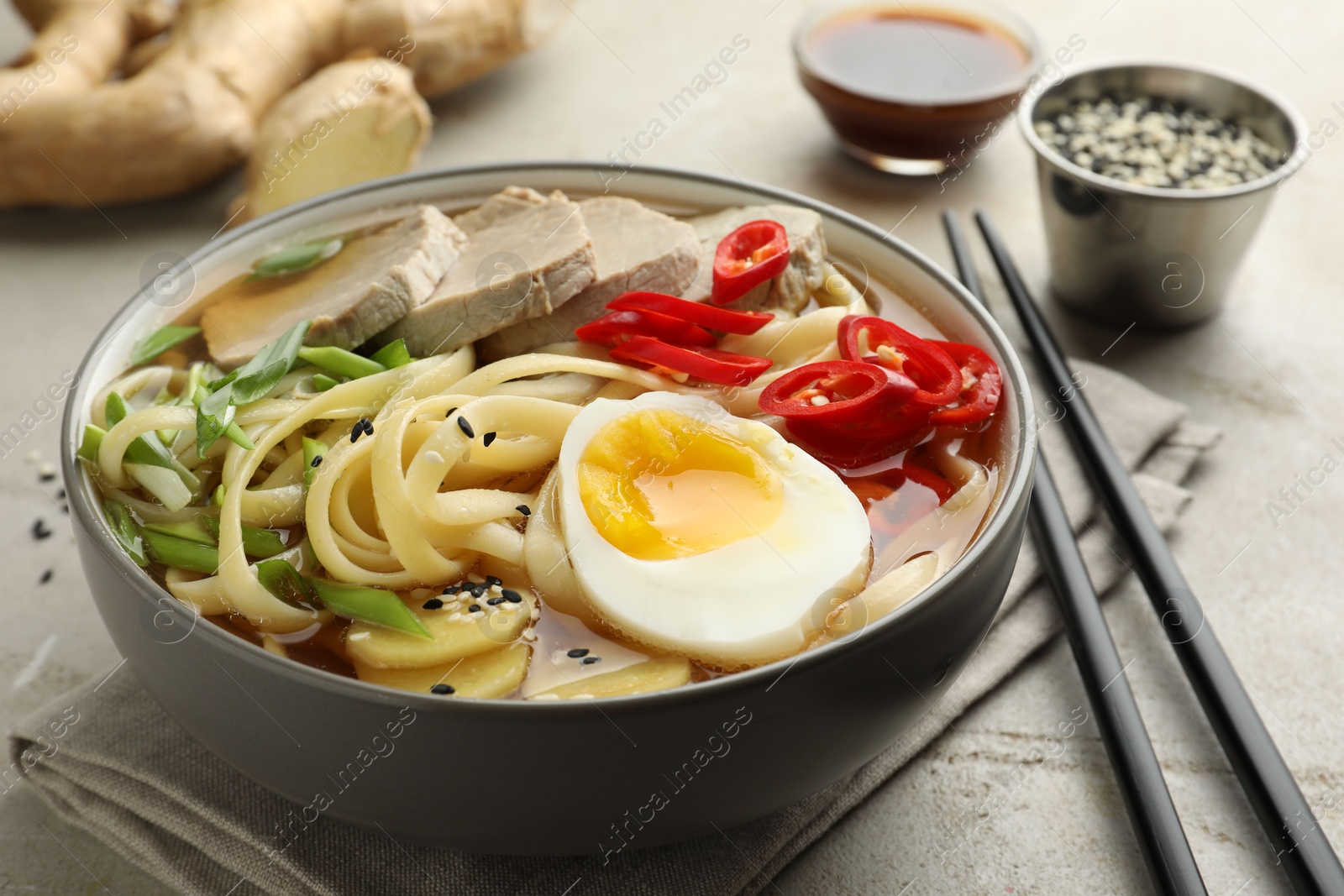 Photo of Delicious ramen in bowl and chopsticks on light textured table, closeup. Noodle soup