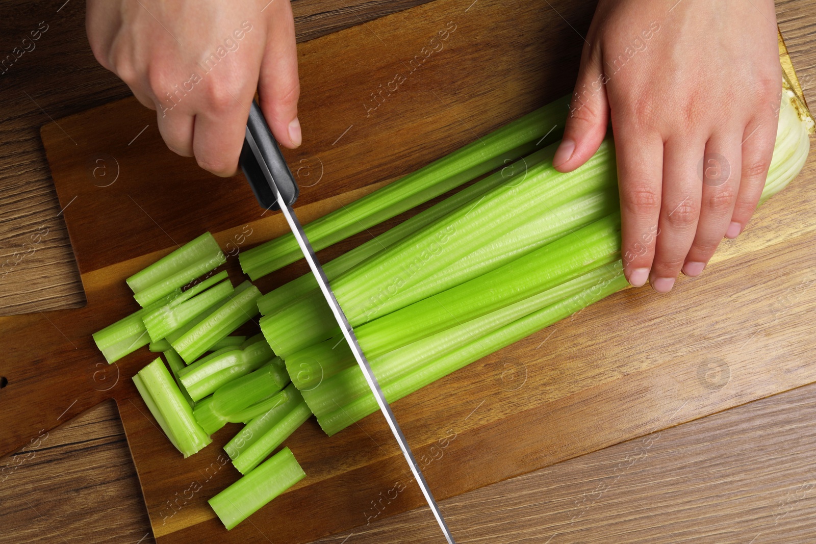 Photo of Woman cutting fresh green celery at wooden table, top view
