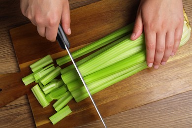 Woman cutting fresh green celery at wooden table, top view