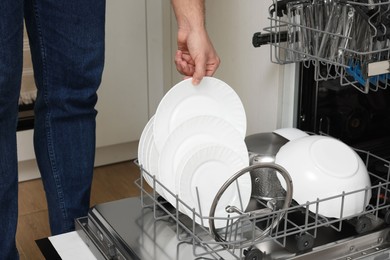 Man loading dishwasher with plates indoors, closeup