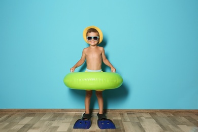 Photo of Cute little boy with inflatable ring wearing flippers near color wall