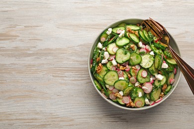 Photo of Bowl of delicious cucumber salad, spoon and fork on white wooden table, top view. Space for text