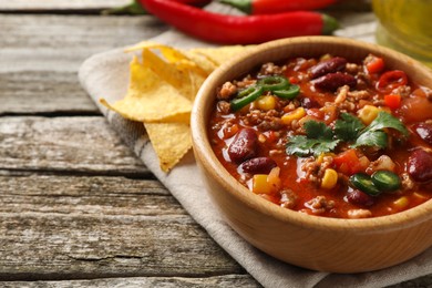 Photo of Bowl with tasty chili con carne and nachos on wooden table, closeup. Space for text