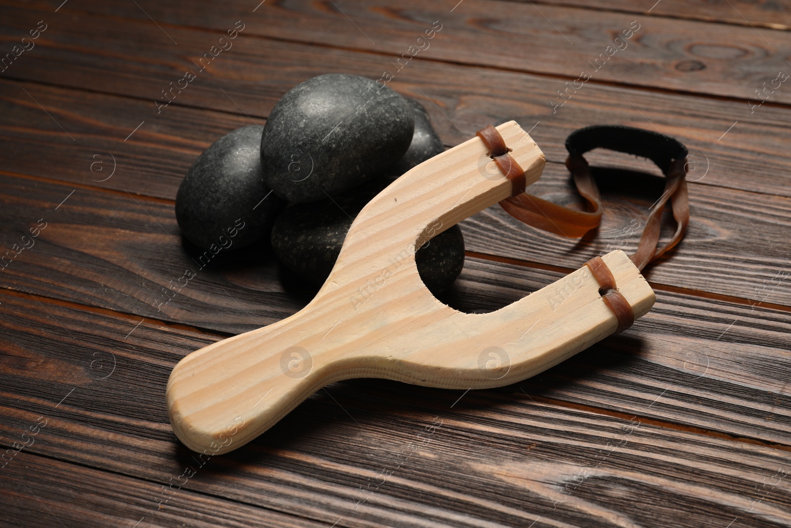 Photo of Slingshot with stones on wooden table, closeup