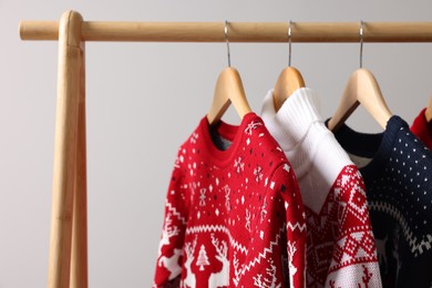 Rack with different Christmas sweaters on light background, space for text