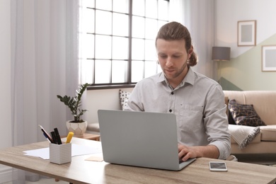 Photo of Young man working with laptop at desk in home office