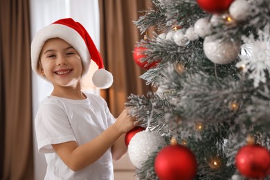 Photo of Cute little girl decorating Christmas tree at home