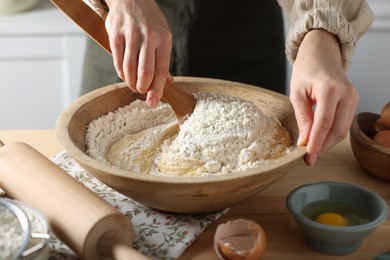 Photo of Woman kneading dough with spoon in bowl at wooden table indoors, closeup