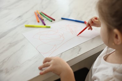 Photo of Little girl drawing with marker at white marble table, closeup