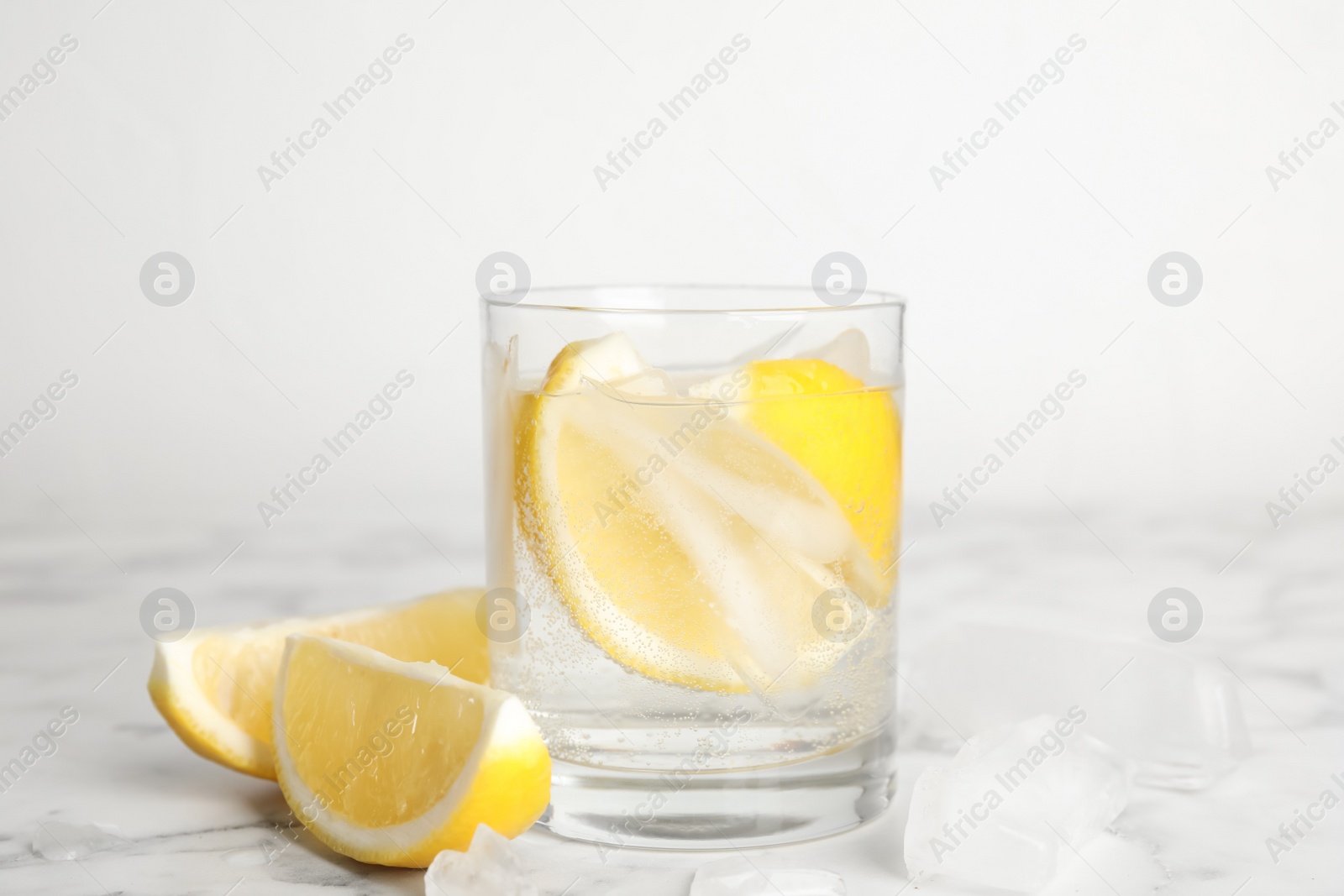 Photo of Soda water with lemon slices and ice cubes on white marble table