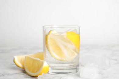 Soda water with lemon slices and ice cubes on white marble table