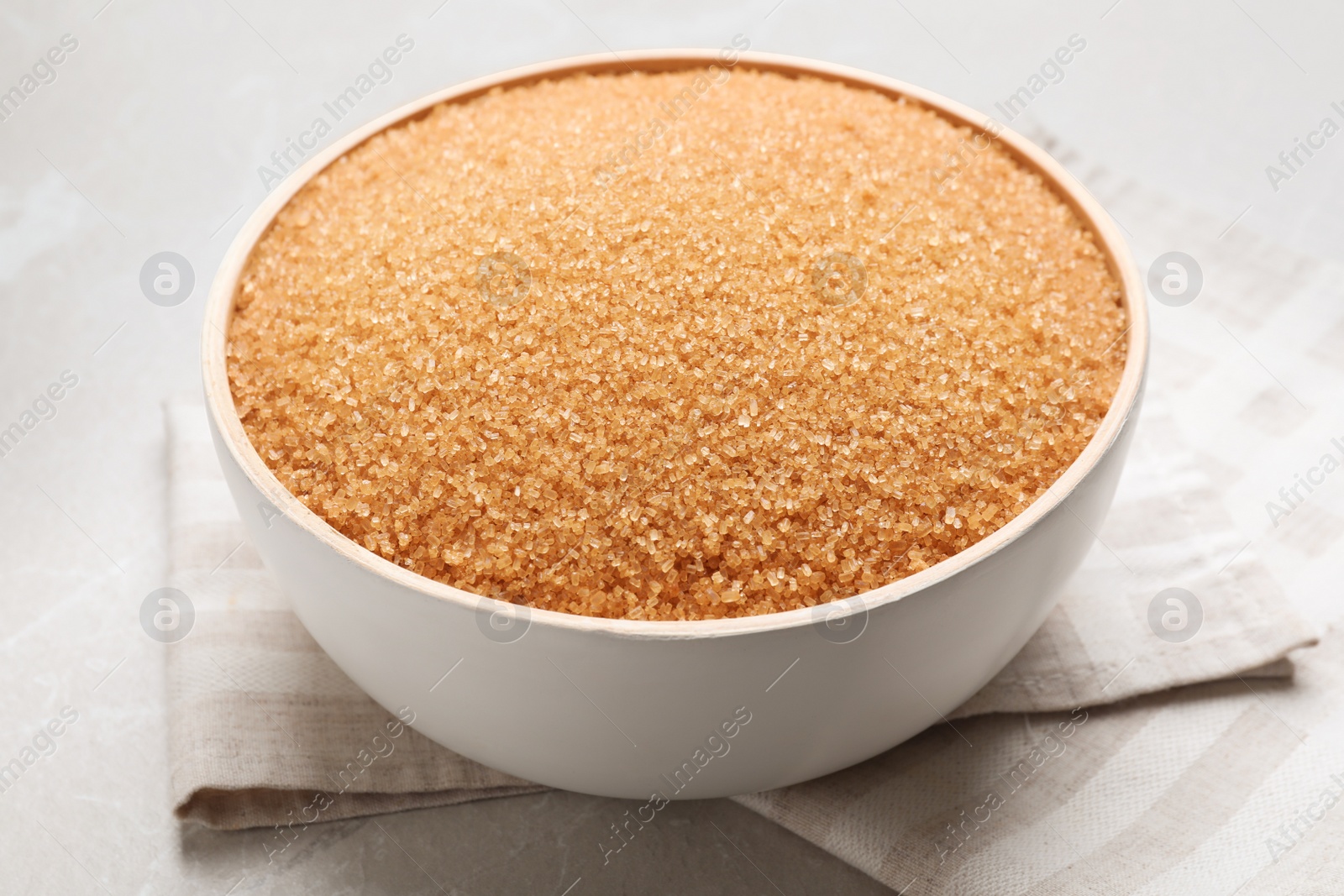 Photo of Brown sugar in bowl on light grey table, closeup