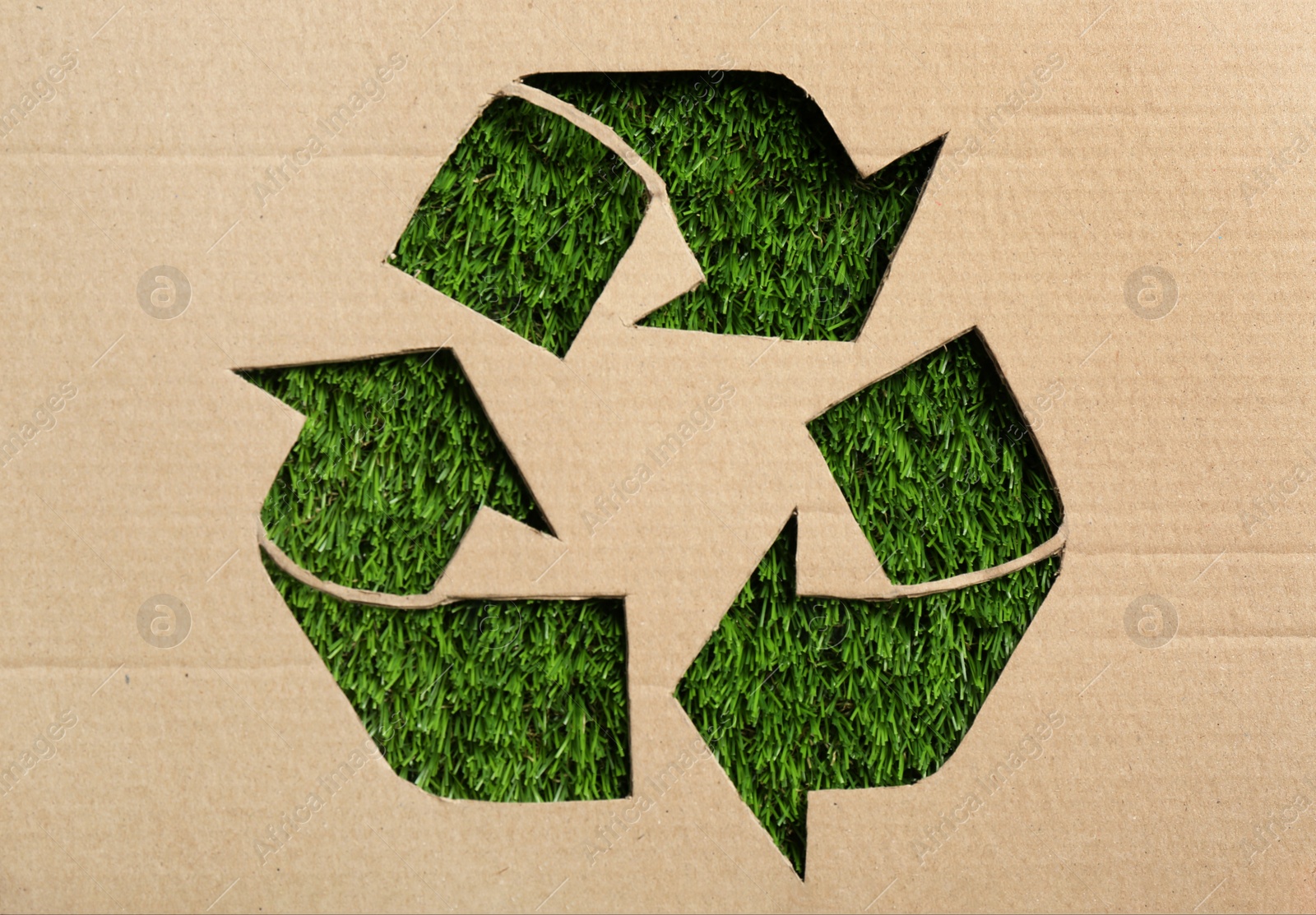 Photo of Sheet of cardboard with cutout recycling symbol on green grass, top view