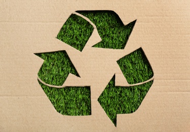 Photo of Sheet of cardboard with cutout recycling symbol on green grass, top view