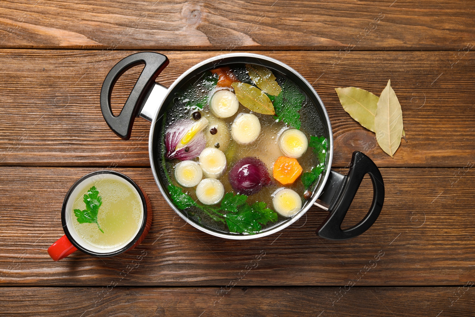 Photo of Tasty bouillon and bay leaves on wooden table, flat lay