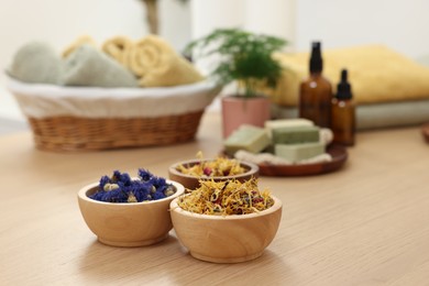 Photo of Bowls of dry flowers on light wooden table, space for text. Spa therapy
