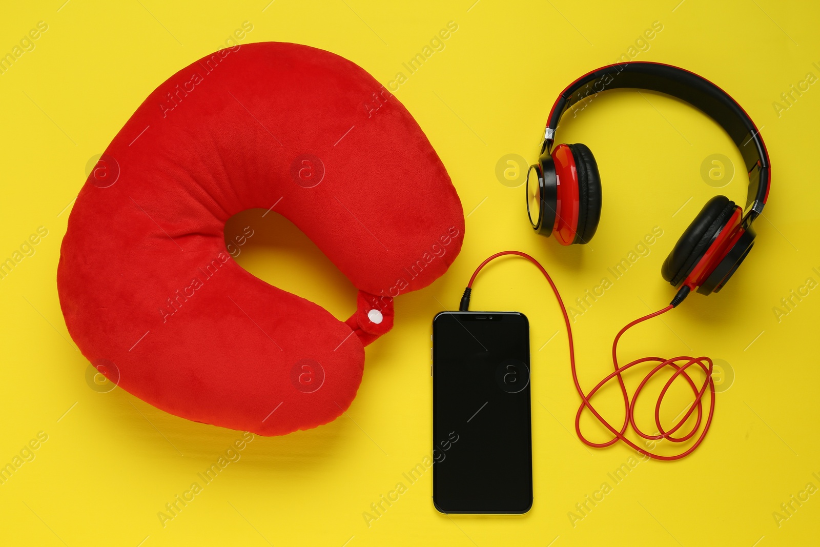 Photo of Red travel pillow, smartphone and headphones on yellow background, flat lay